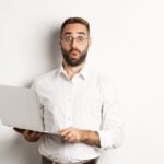 Business. Surprised business man holding laptop and looking interested, standing with computer against white background.